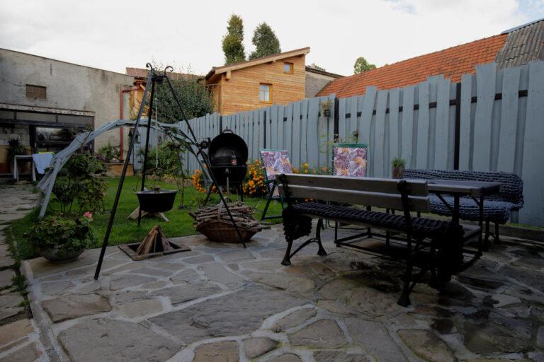 A photo showing a corner of the yard. A barbecue, a fire pit, and a relaxation area with a small garden.